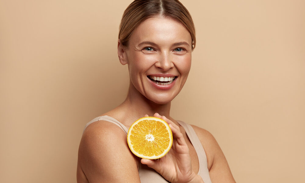 Vrouw met zomerse glow glimlacht met een sinaasappel